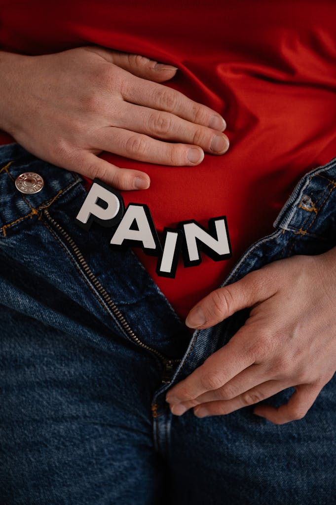 Close-up of a person in jeans holding their stomach with 'PAIN' text overlay.